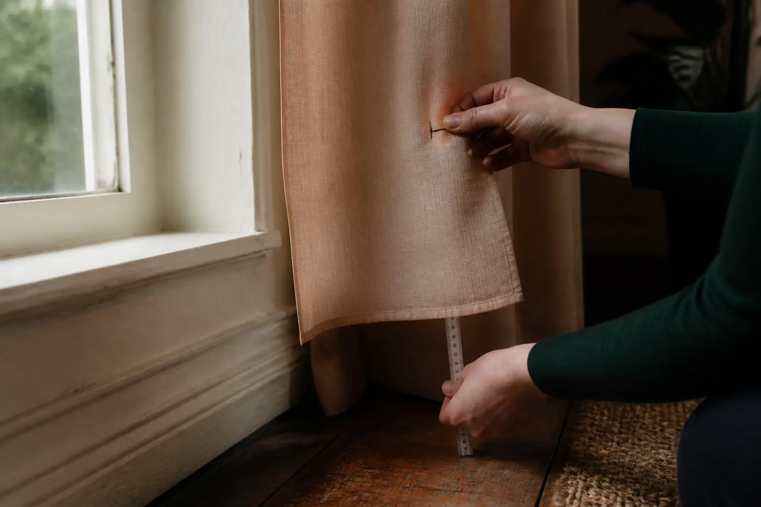 Rideaux trop long astuces : mains mesurant l’ourlet d’un rideau trop long près de la fenêtre, lumière douce naturelle.