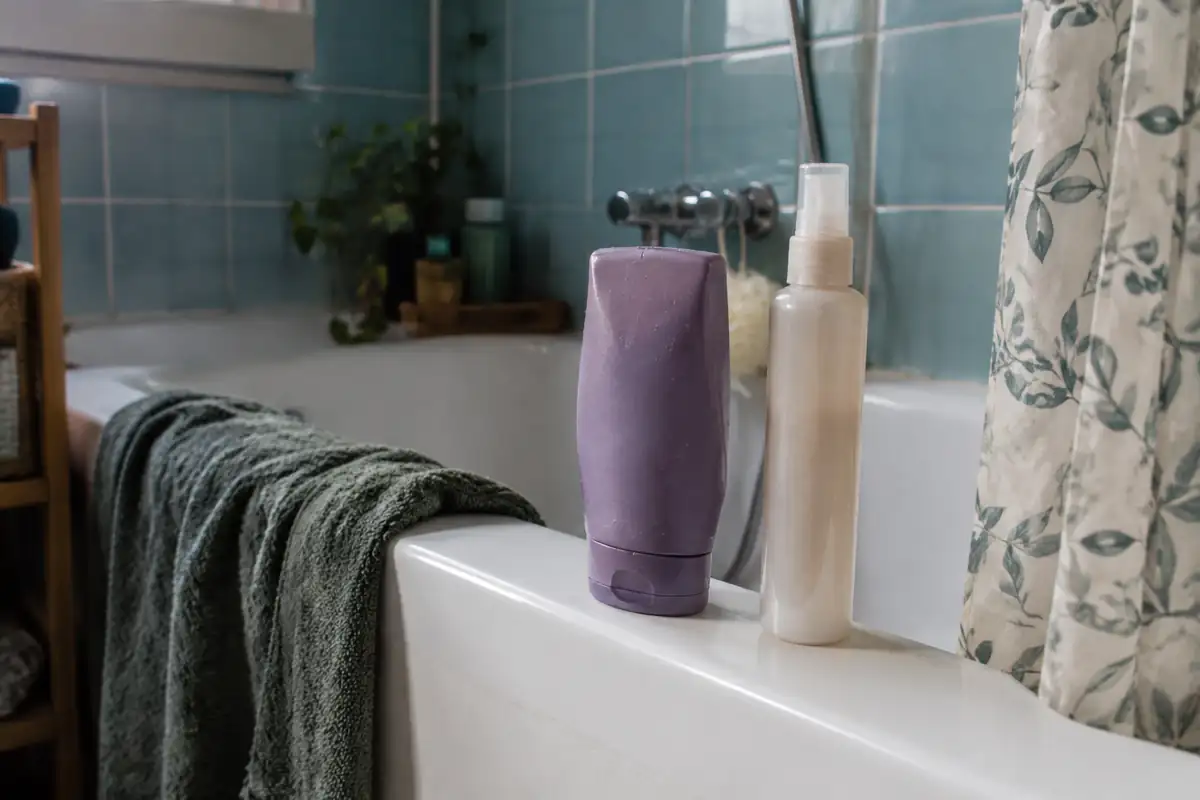 Après-shampooing et flacon de leave-in alignés sur le bord d'une baignoire